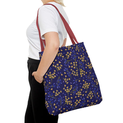 A person carries a Floral Tote Bag with burgundy-red straps and a navy-blue body adorned with yellow and blue botanical sprigs, perfect for vibrant summer outings or cheerful market trips.