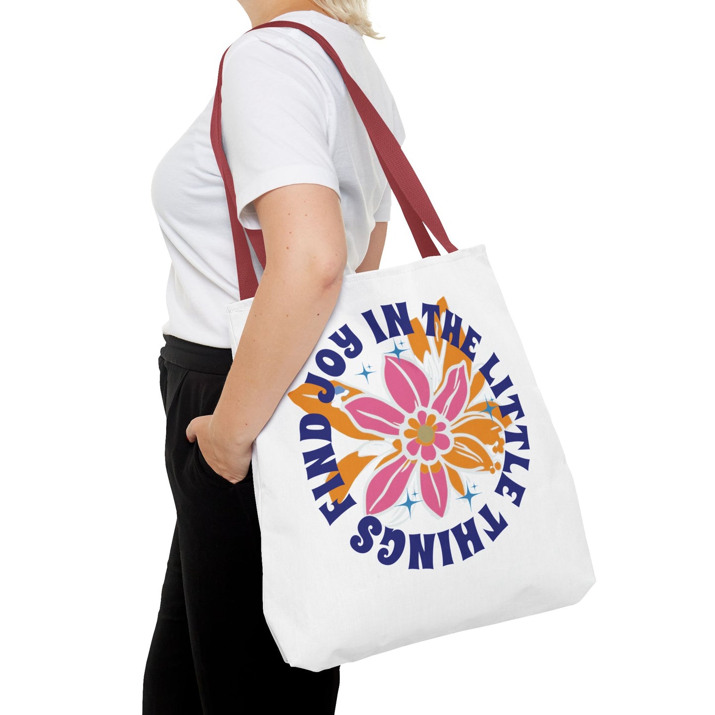 A woman holds the Find Joy in Little Things tote bag, featuring a colorful flower design, embodying positivity and versatility for everyday use.