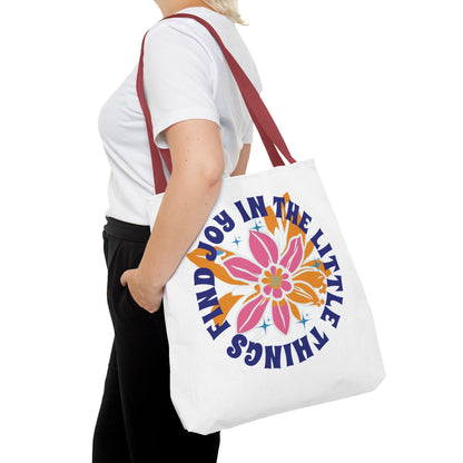 A woman holds the Find Joy in Little Things tote bag, featuring a colorful flower design, embodying positivity and versatility for everyday use.
