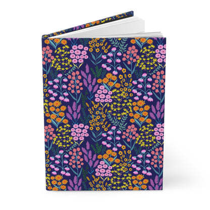 HARDCOVER JOURNAL, MATTE, RULED, 5X7, SEWN BIND, CLEAN-TEAR PAGES - FLORAL MEADOWS, BLUE BACKGROUND, featuring a dense floral design, stands upright with slightly fanned pages showcasing its quality craftsmanship.