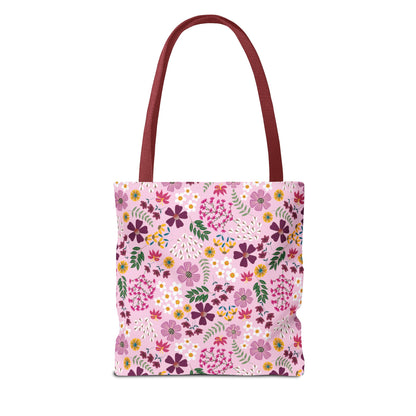 The Rose Garden Blush Tote Bag features burgundy-red handles and a pink floral-patterned body with purple, magenta, yellow, and white blossoms, embodying FireBrook Designs' commitment to stylish, durable everyday accessories.