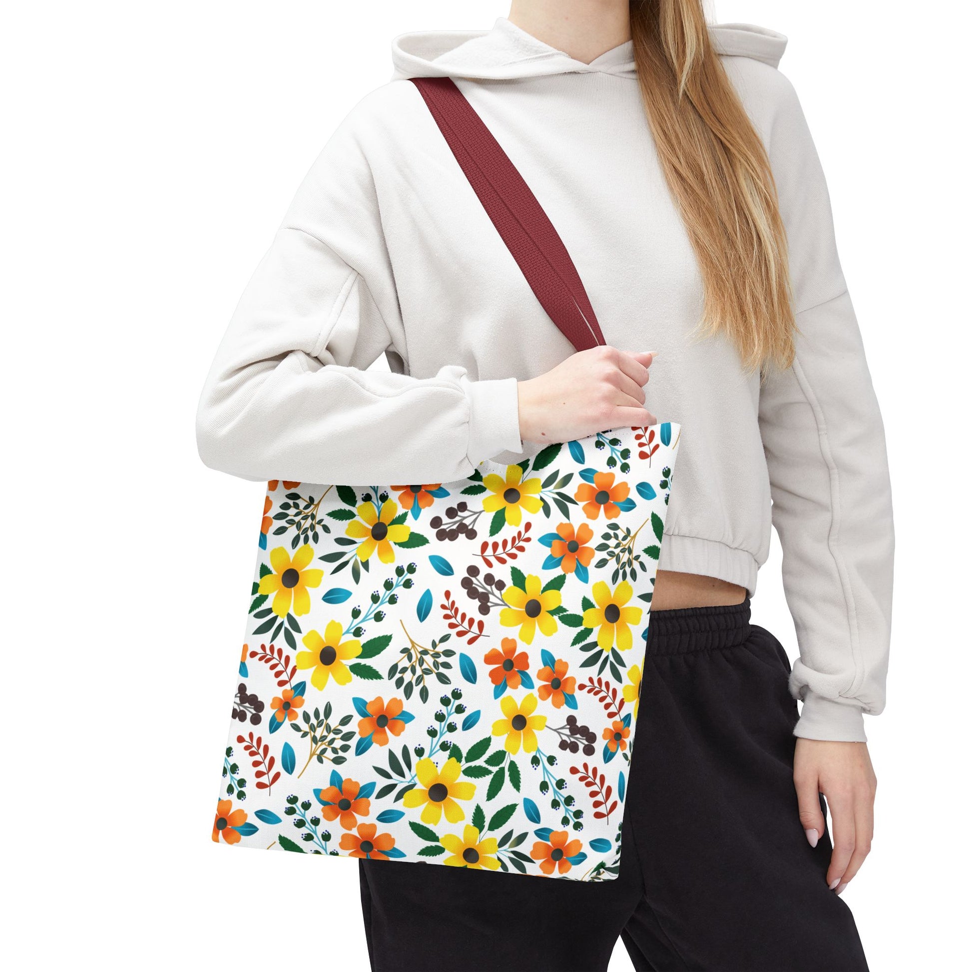 Floral Tote Bag featuring a vibrant yellow, orange, and green floral print on a white background with a burgundy-red strap, ideal for summer outings, carried by a person in a light cropped hoodie.