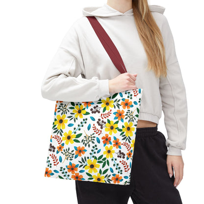 Floral Tote Bag featuring a vibrant yellow, orange, and green floral print on a white background with a burgundy-red strap, ideal for summer outings, carried by a person in a light cropped hoodie.