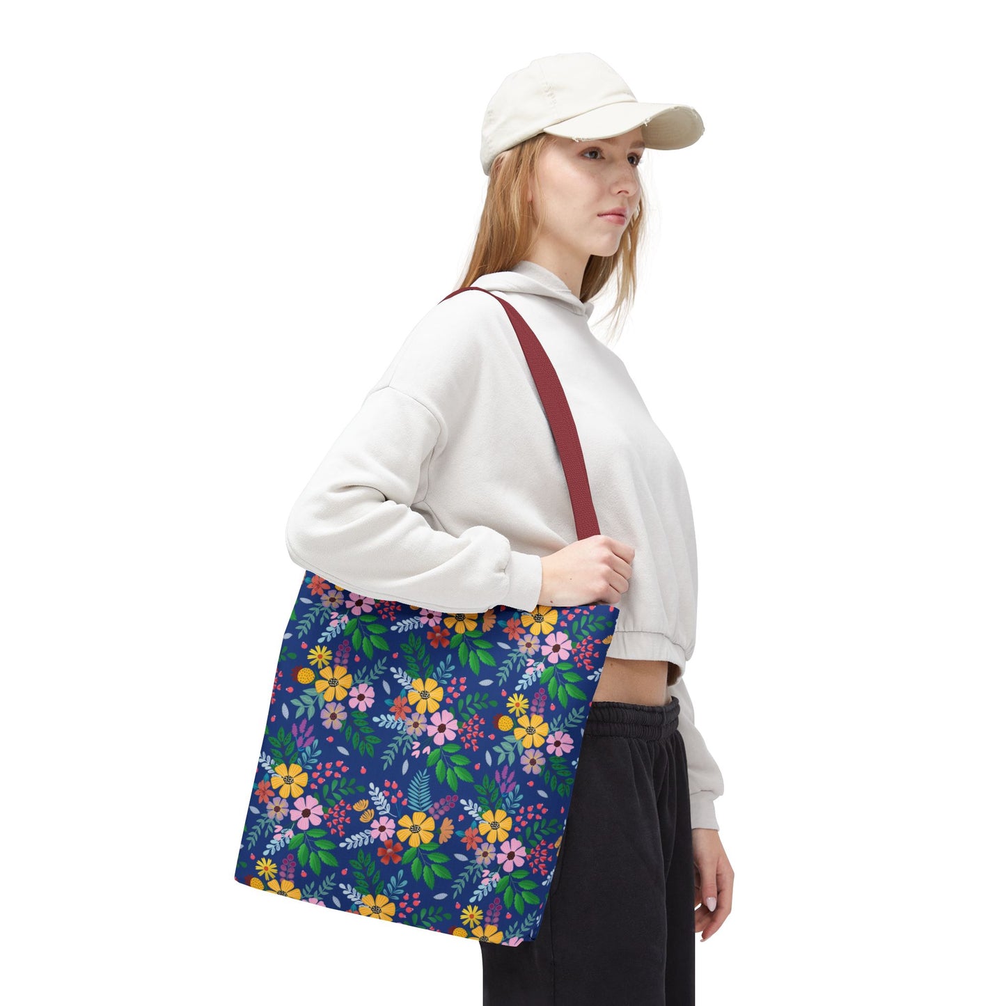 Young woman models the Floral Tote Bag, featuring a dark blue background with colorful floral patterns, ideal for summer outings. The tote complements her casual outfit, embodying FireBrook Designs' joyful and stylish essence.