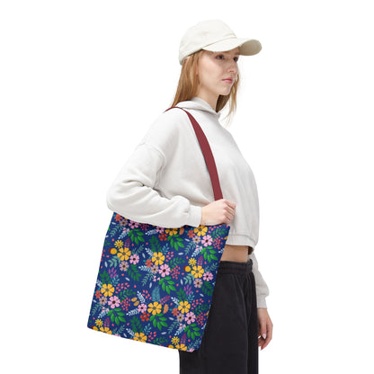 Young woman models the Floral Tote Bag, featuring a dark blue background with colorful floral patterns, ideal for summer outings. The tote complements her casual outfit, embodying FireBrook Designs' joyful and stylish essence.