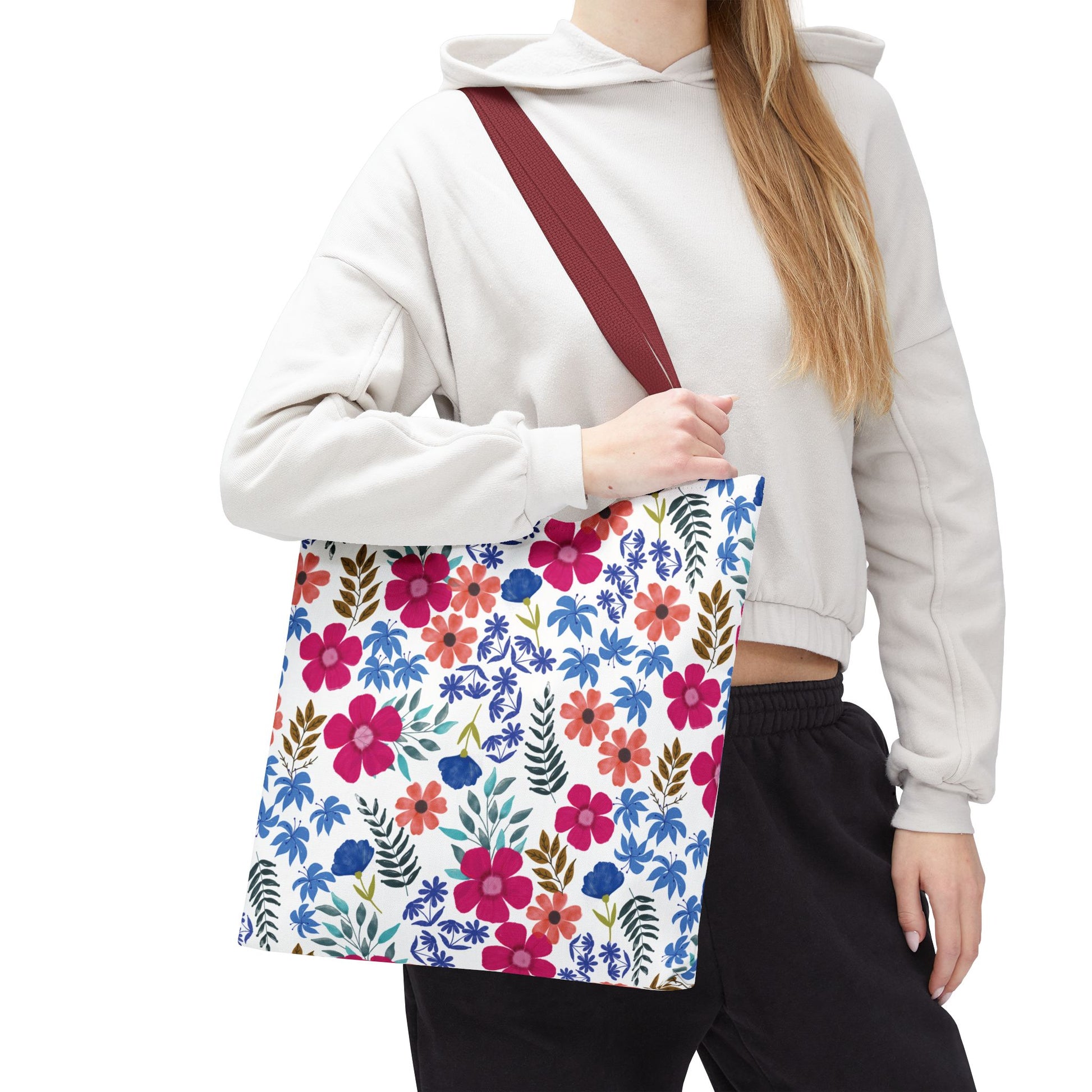Floral Tote Bag featuring a vibrant pink, red, and blue blossom pattern with leafy accents on a white background, carried by a casually dressed person, showcasing its spacious design and burgundy strap.