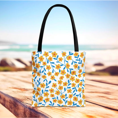 Floral Tote Bag on wooden surface with black straps, featuring yellow-orange flowers and blue stems, ideal for summer outings, embodying FireBrook Designs' uplifting style and joyful, practical design.