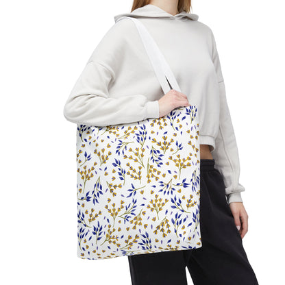 Person carrying the Floral Tote Bag, featuring a cheerful yellow and blue botanical pattern, ideal for summer outings. The tote complements their light cropped hoodie and dark pants ensemble.
