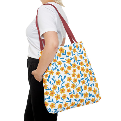Person wearing a white T-shirt holds the Buttercup Cream Tote Bag, featuring a lively pattern of yellow flowers and blue stems, complemented by dark red straps, embodying joyful FireBrook Designs' aesthetic.