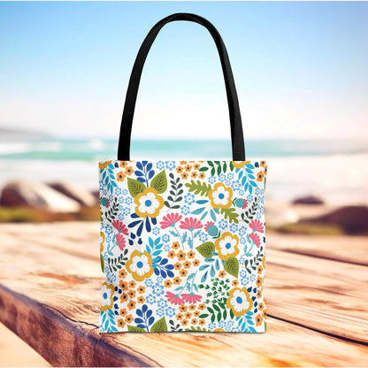 Floral Tote Bag on a wooden surface with a vibrant floral pattern, featuring durable black straps. Ideal for adding a cheerful touch to summer outings, embodying FireBrook Designs' uplifting style.
