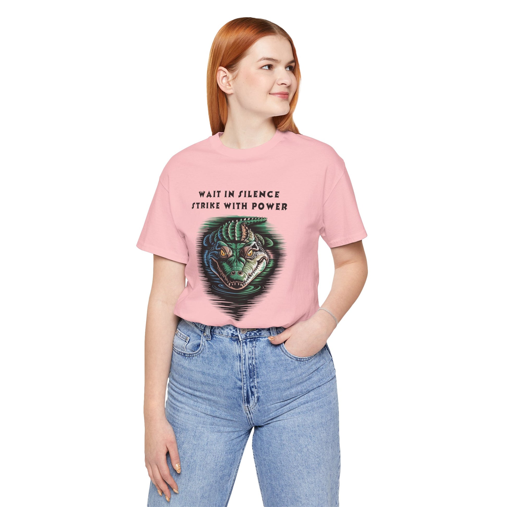 Crocodile: Walk in Silence, Strike with Purpose Bella+Canvas Unisex T-Shirt featuring a woman in a pink shirt and jeans, posing with a detailed crocodile design, reflecting bold, unique style.