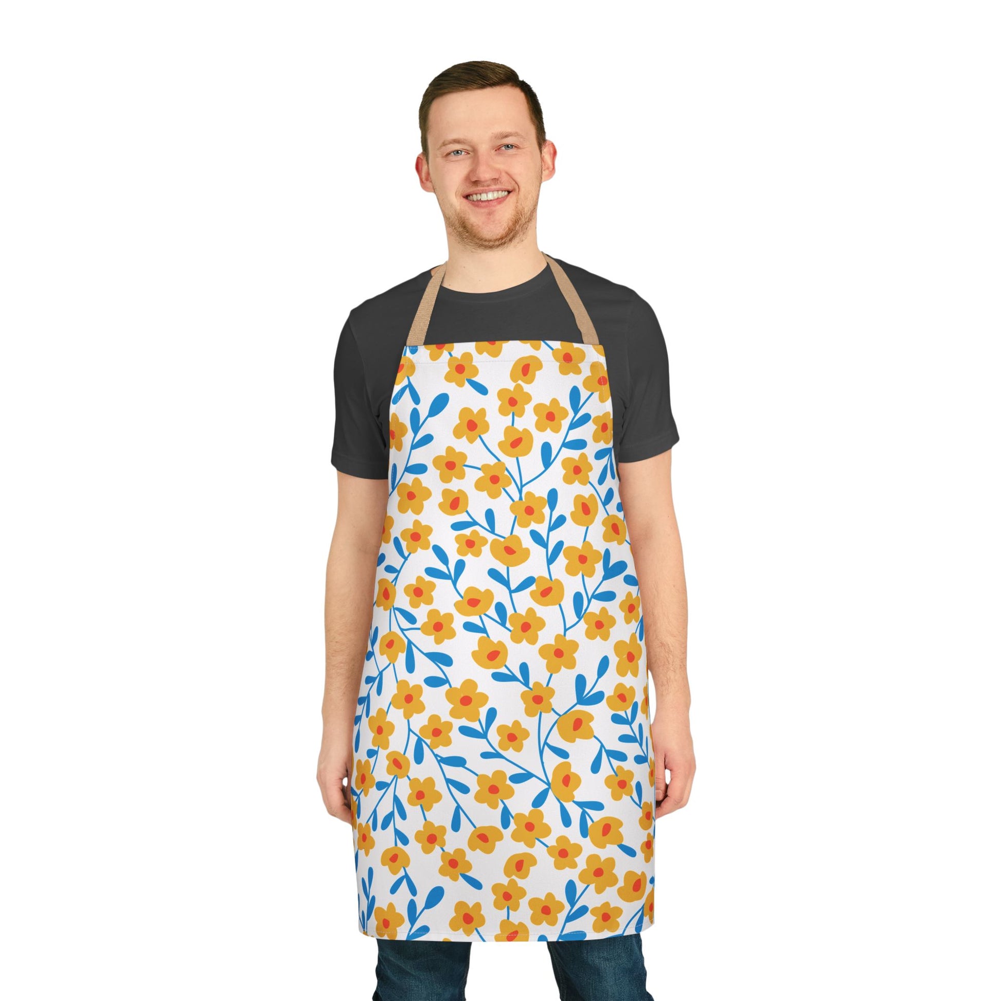 Smiling man wearing the Floral Apron, featuring yellow-orange flowers and blue leaves. Made from soft polyester canvas, it's stain-free, ideal for cooking. The apron has tan straps and tie-back closure.