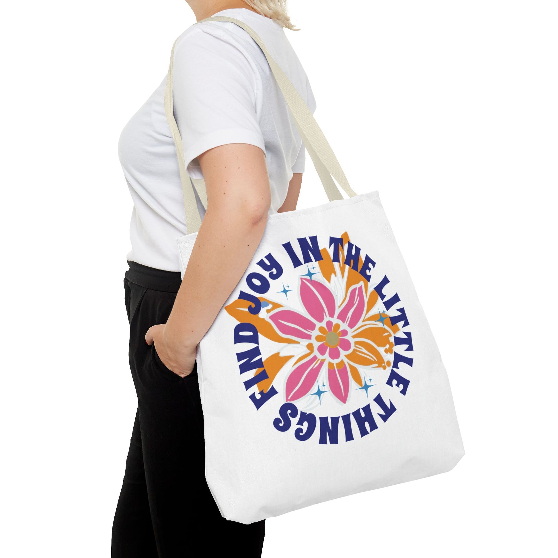 Woman holding the Find Joy in Little Things tote bag featuring a colorful flower design, ideal for spreading positivity and carrying essentials.