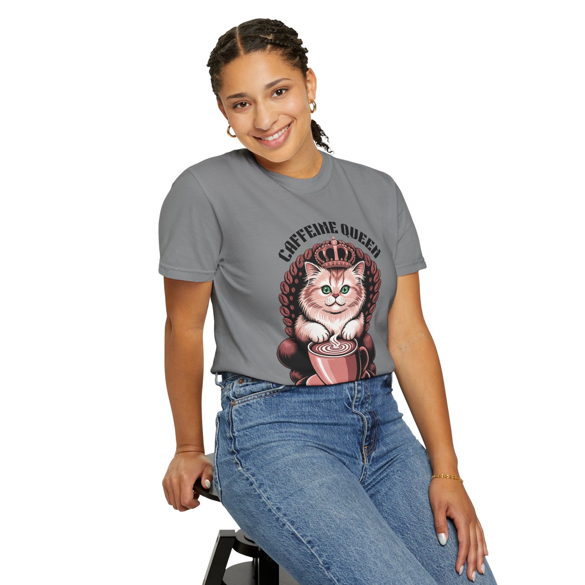 Cat Caffeine Queen T-shirt showcased by a smiling woman sitting on a stool. The shirt features a fun, playful design with a cat wearing a crown, ideal for cat and coffee enthusiasts.