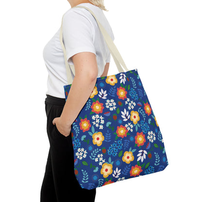 Person wearing a white T-shirt and black pants carries the Cornflower Patch Tote Bag, featuring a bright blue background with a vibrant floral pattern, ideal for cheerful and stylish summer outings.
