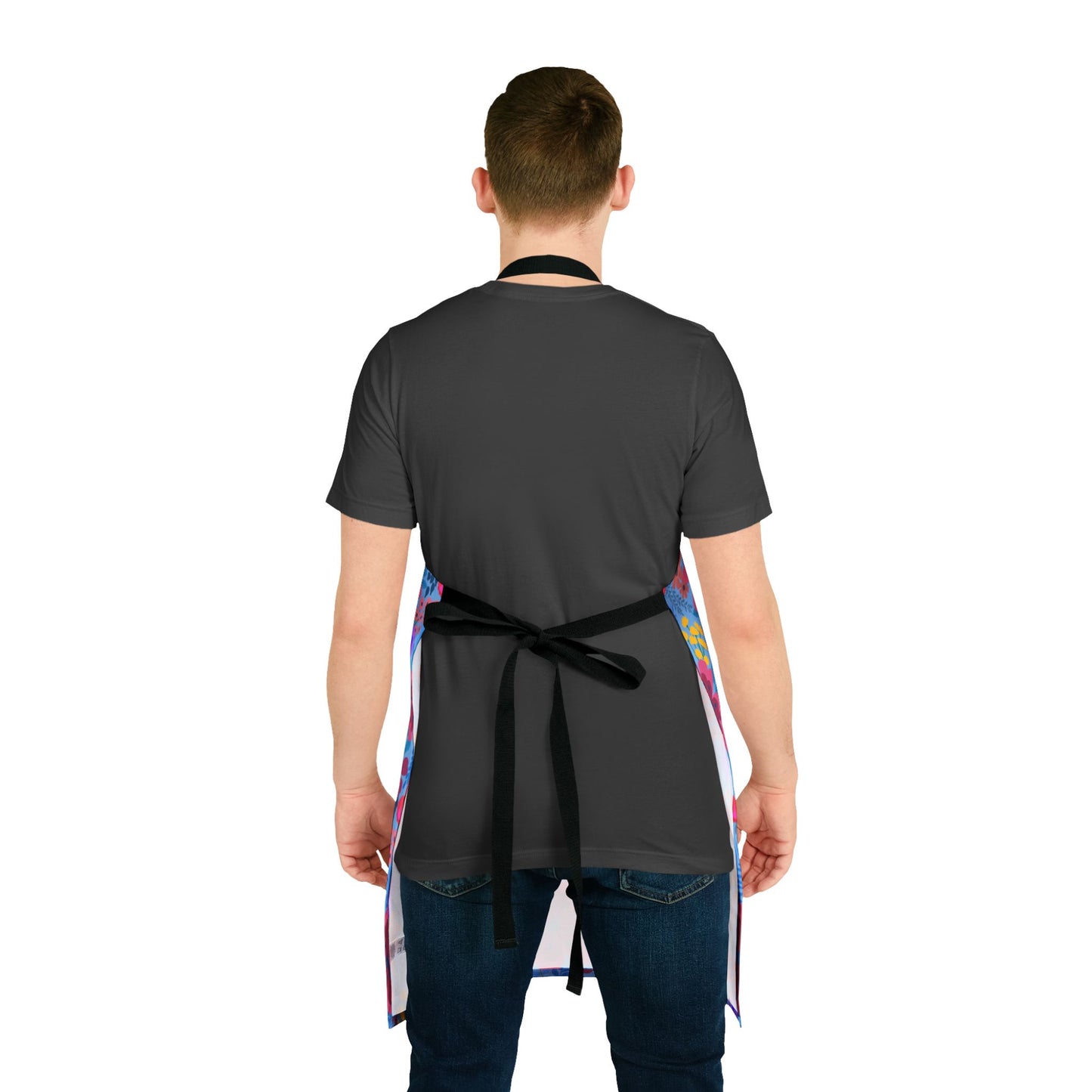 A person wears a Floral Apron with vibrant patterns over a dark gray T-shirt and blue jeans. The apron, from FireBrook Essentials, combines style and comfort, ideal for various activities.