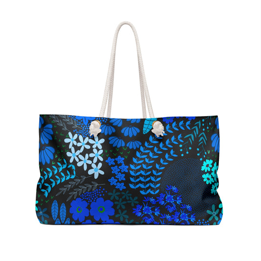 Floral Weekender Bag: A large tote with blue and teal floral patterns on a black background, featuring sturdy white rope handles. Ideal for stylish, practical getaways, embodying FireBrook Designs' comforting and uplifting aesthetics.