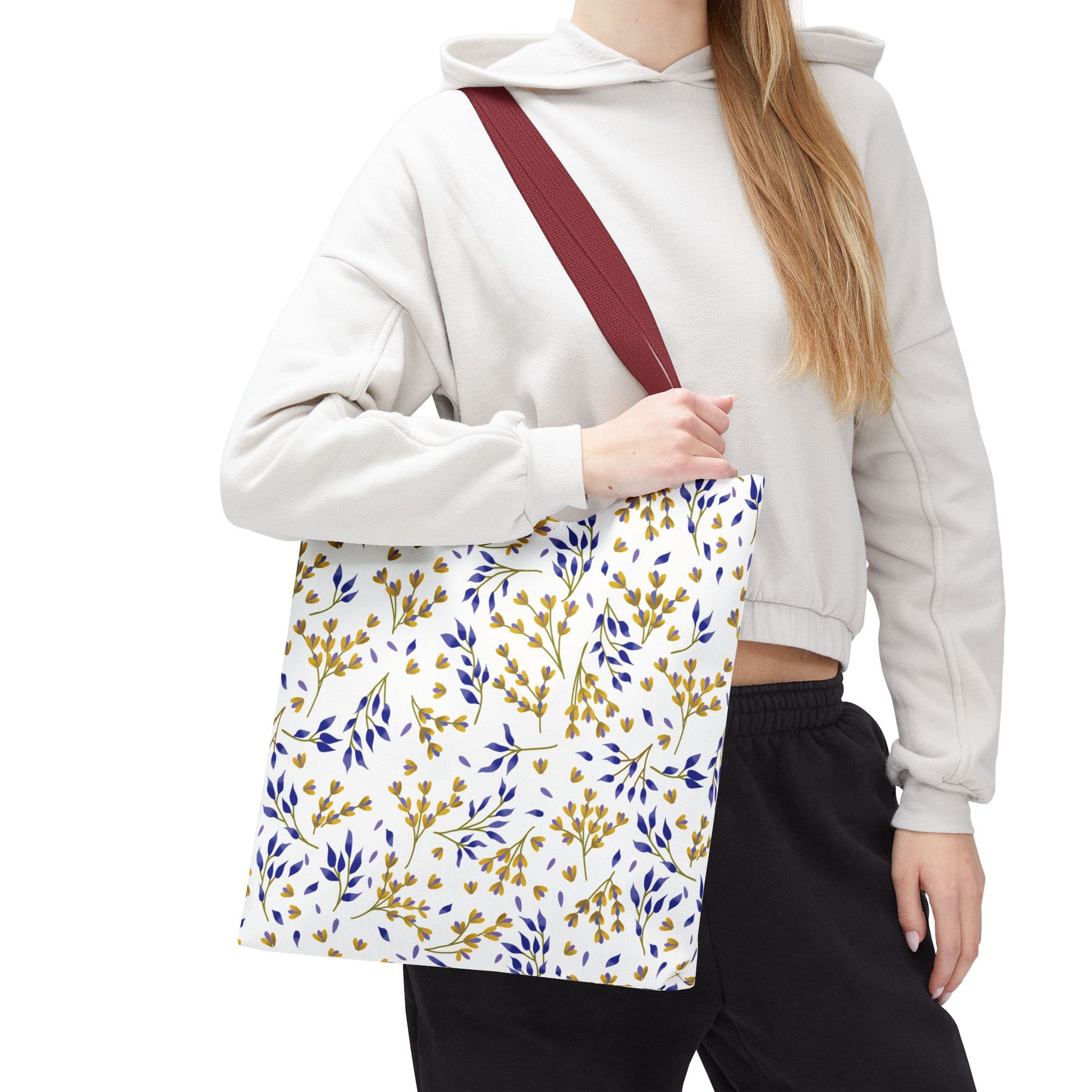 A person carries the Floral Tote Bag from FireBrook Designs, featuring a white body with mustard-yellow and deep-blue botanical patterns, burgundy straps, perfect for summer outings and vibrant style.