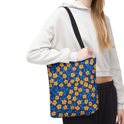 Person wearing a light hoodie and dark pants holds the Cobalt Poppy Field Tote Bag, adorned with yellow-orange flowers and blue leaves, perfect for joyful, stylish summer outings.