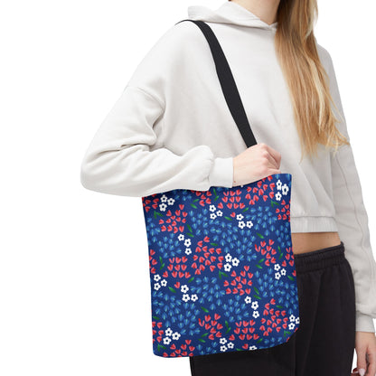 Berry Blue Festival Tote Bag with a navy-blue floral design, carried by a person in a light hoodie. Ideal for cheerful summer outings, the bag features durable polyester, reinforced handles, and ample boxed corners.