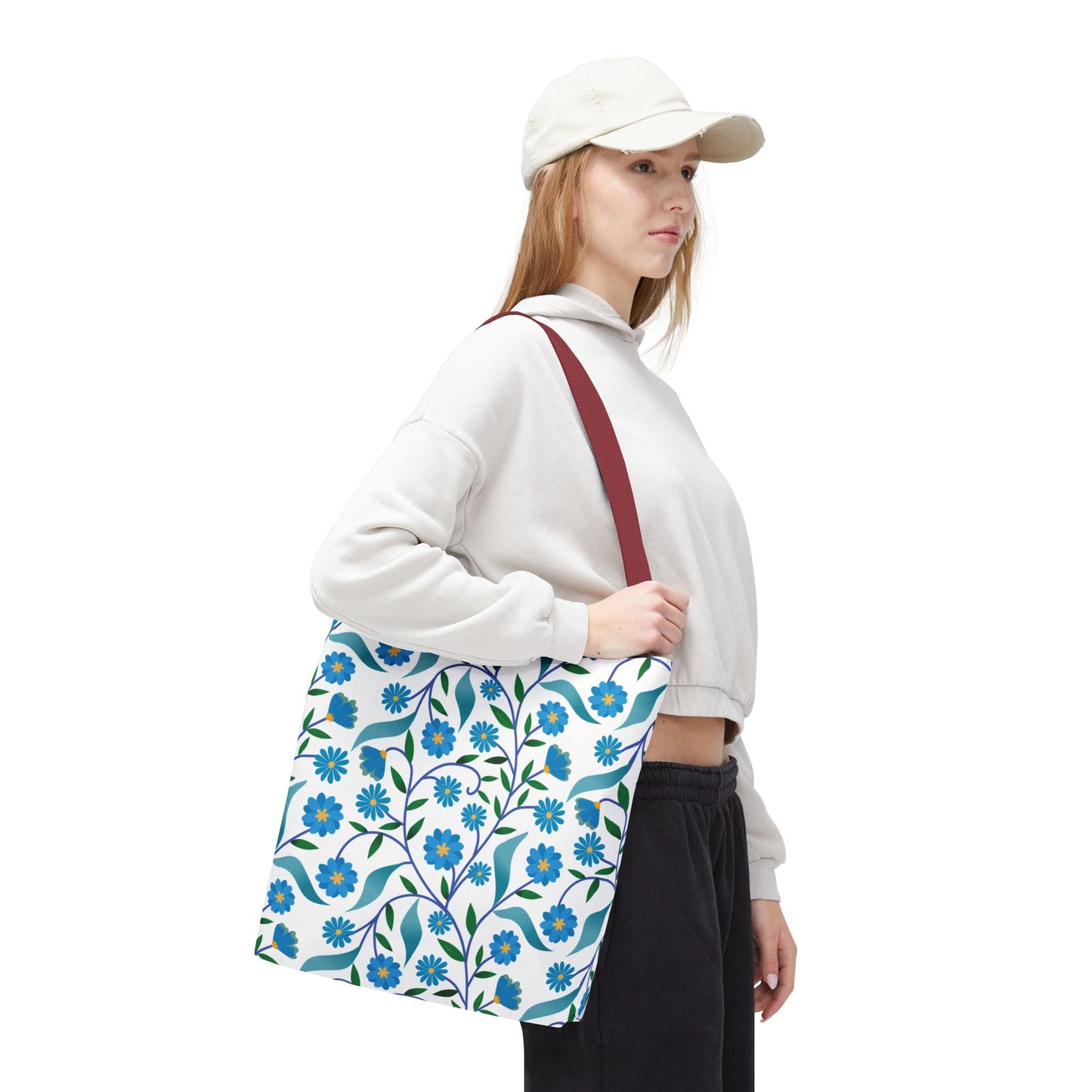 Blue Floral Tote Bag modeled by a young woman. The white canvas features a blue flower and green leaf pattern with a burgundy strap, embodying FireBrook Designs' uplifting, joyful style.