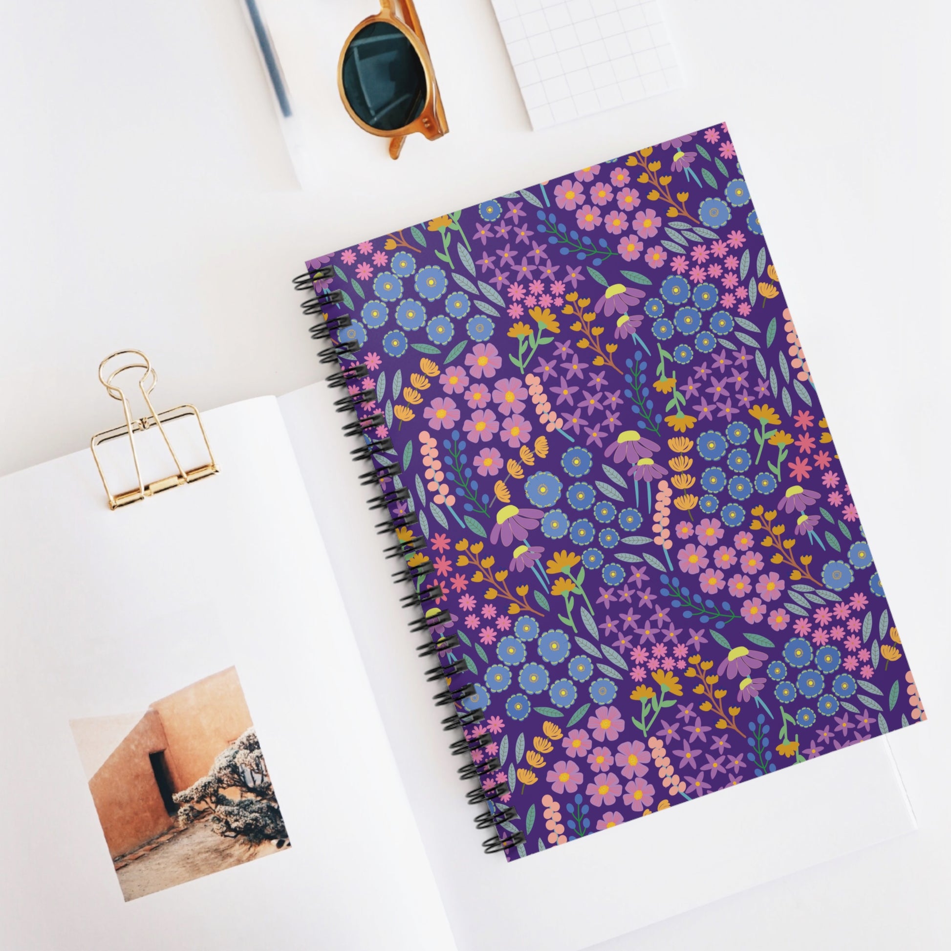Floral Spiral Notebook with vibrant hand-drawn flowers on a purple cover, centered on a clean white desk alongside stylish stationery, embodying FireBrook Designs' blend of creativity and functionality.