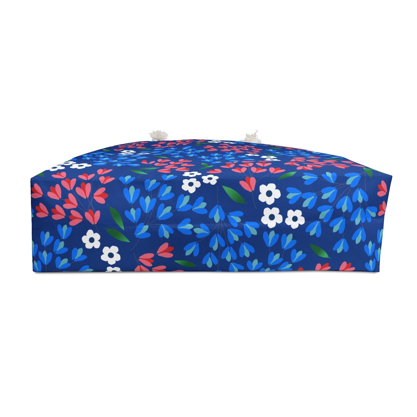 Weekender Bag: A low, rectangular pouf with a mid-blue fabric featuring stylized blossoms and leaves, complete with domed top, tassels, and box-shaped sides. Perfect for stylish, joyful travel.