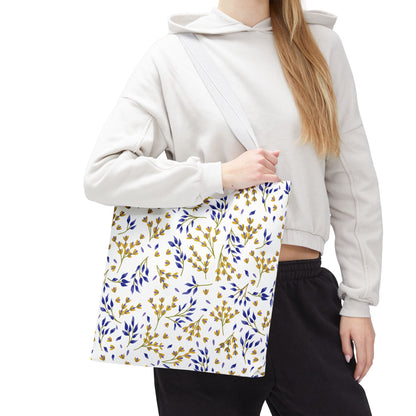 Person wearing a light hoodie and dark pants, holding a Floral Tote Bag with a white background, yellow blossoms, and blue leaves pattern, ideal for summer outings.