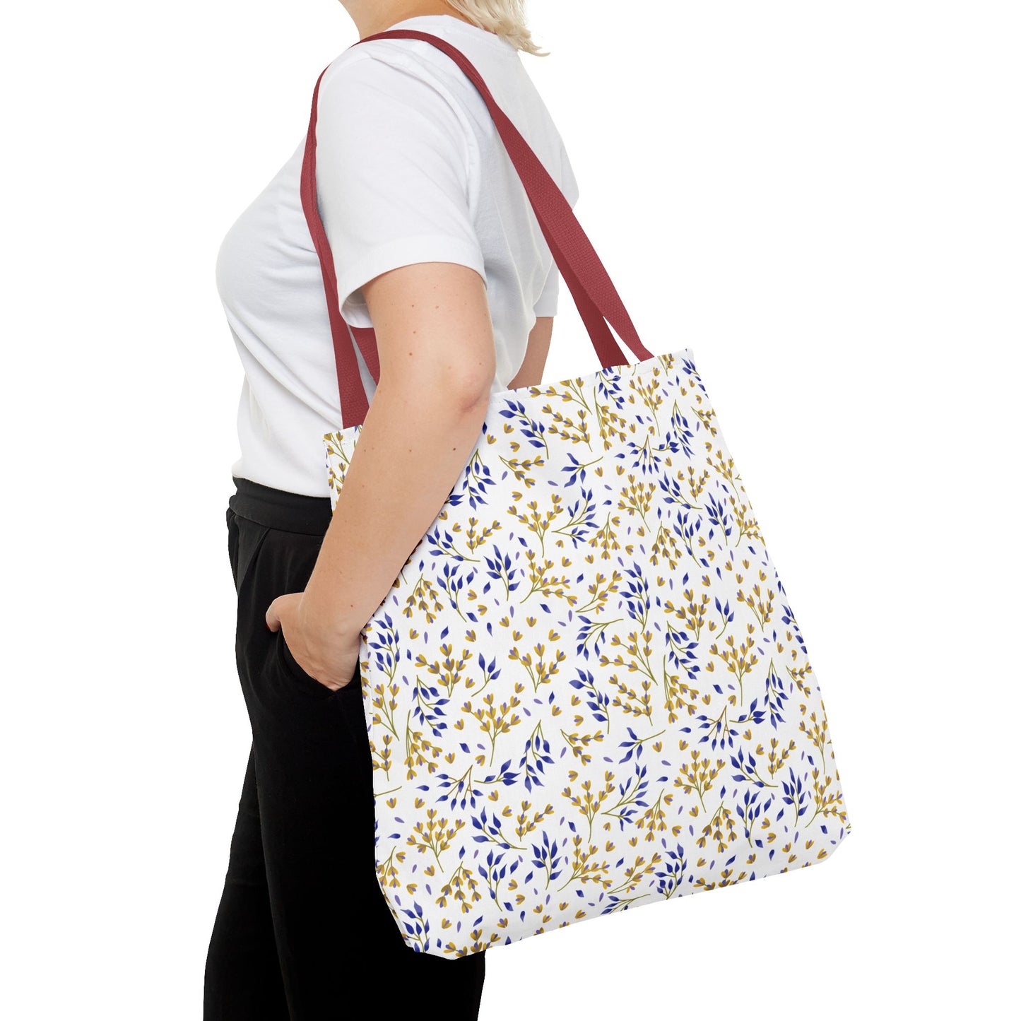 A person wears a plain white T-shirt, black pants, and carries the Wild Herb Garden Tote Bag featuring dark-red straps and a bright botanical print, perfectly embodying FireBrook Designs' uplifting and joyful style.