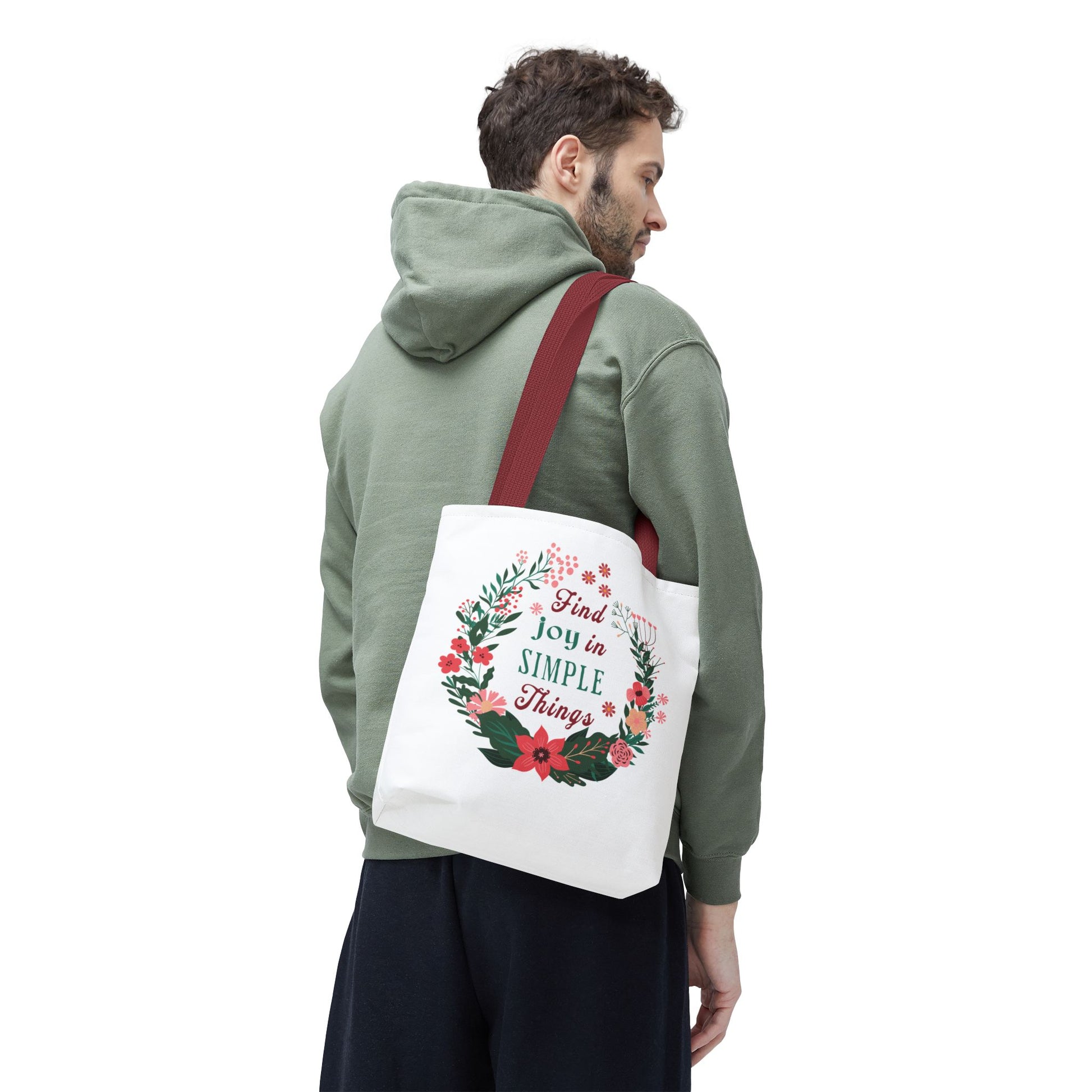 Man in green sweatshirt carrying 'Find Joy in Simple Things' tote bag with floral design, ideal for versatile, stylish use.