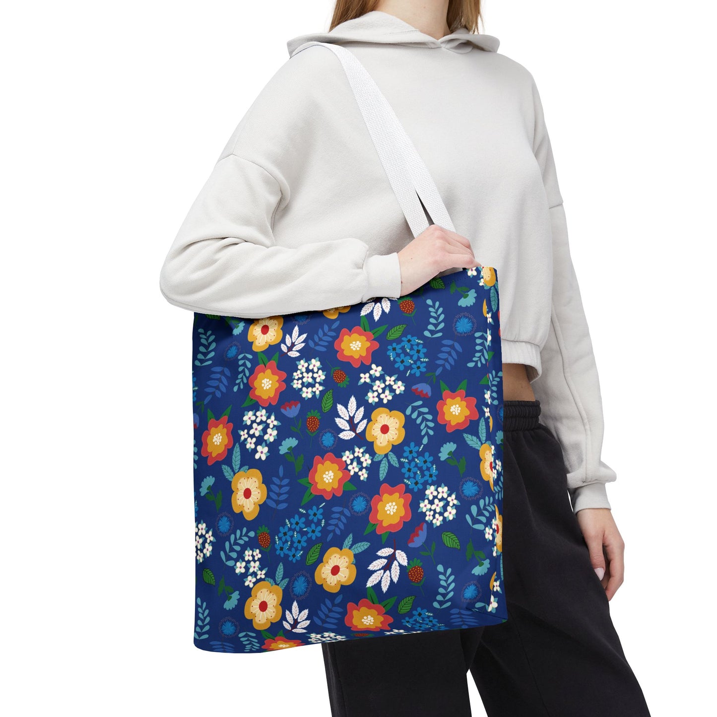 Floral Tote Bag slung over shoulder, featuring vibrant red, yellow, and white blossoms on a deep blue background, ideal for summer outings. Its durable design aligns with FireBrook Essentials' joyful, uplifting aesthetic.