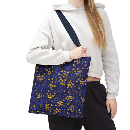 Person wearing a light-colored hoodie and dark pants holds a Floral Tote Bag with a navy background and golden-yellow leafy pattern, ideal for cheerful summer outings and available from FireBrook Designs.