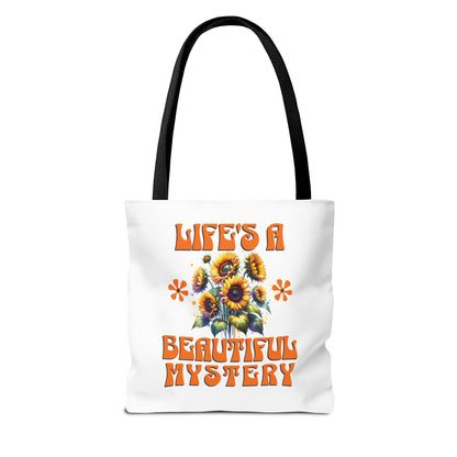 Life's A Beautiful Mystery Tote Bag features a white design with orange text and floral patterns, complemented by a black strap, embodying FireBrook Essentials' uplifting and stylish approach.