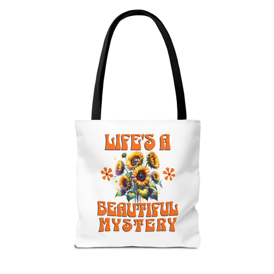 Life's A Beautiful Mystery Tote Bag features a white design with orange text and floral patterns, complemented by a black strap, embodying FireBrook Essentials' uplifting and stylish approach.