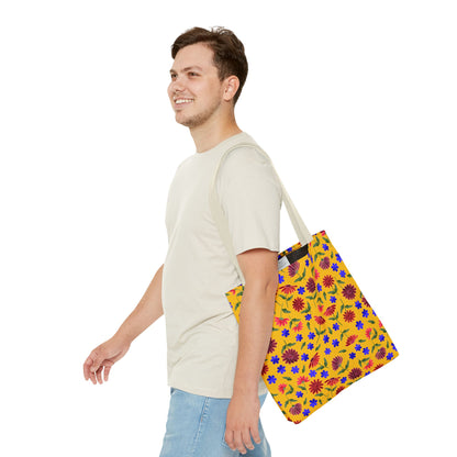 Golden Wildflower Tote Bag: A young man models this vibrant tote, featuring a yellow backdrop with red, blue, and green floral patterns. The bag's sturdy black straps and spacious design add practicality and style.