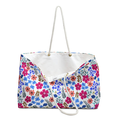 Weekender Bag featuring a vivid floral pattern with pink, coral, blue, and green hues on a white canvas-like material, showcasing sturdy white rope handles and a spacious interior, ideal for stylish travel.