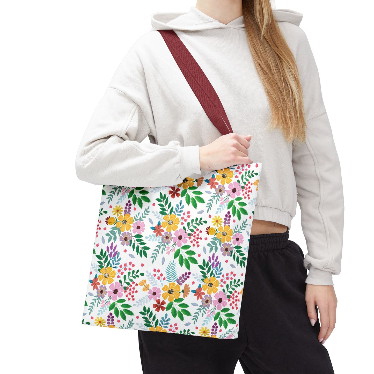 The Spring Floral Patch Tote Bag, featuring vibrant yellow, pink, purple, and red floral patterns on white, is held by a person in casual attire, showcasing its burgundy strap and spacious design.