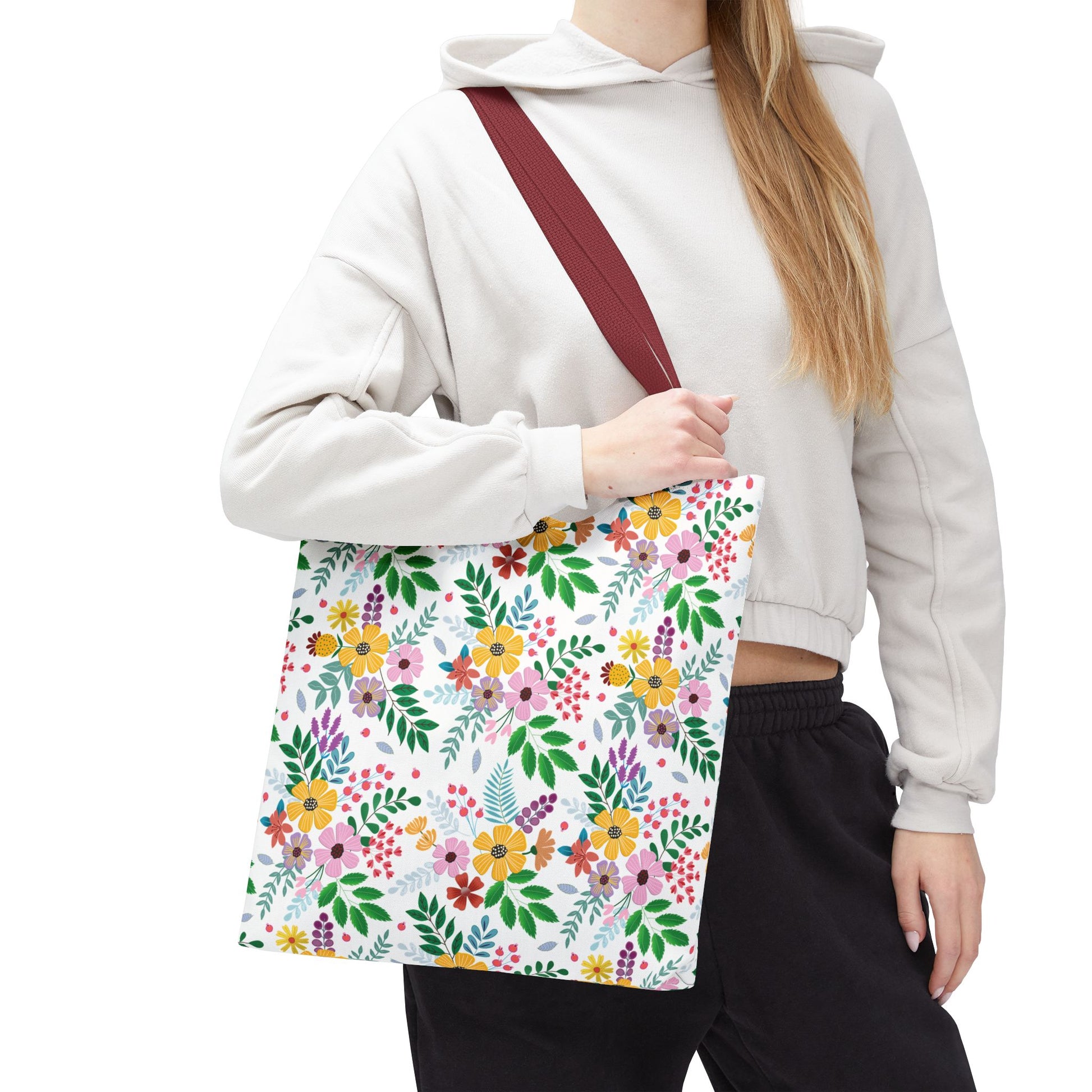 The Spring Floral Patch Tote Bag, featuring vibrant yellow, pink, purple, and red floral patterns on white, is held by a person in casual attire, showcasing its burgundy strap and spacious design.