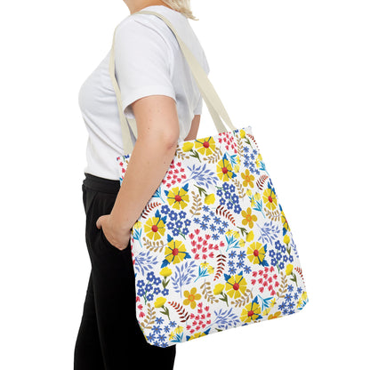 A person carries a Floral Tote Bag, featuring vibrant blossoms and green leaves. This FireBrook Designs accessory blends style and joy, perfect for summer outings and embodying cheerful, original design.