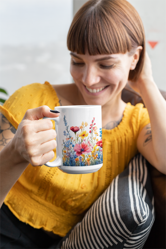 Wildflowers Mug (15oz) held by a woman, showcasing a vibrant floral design. Made from durable ceramic, it complements joyful gatherings, perfect for enhancing your coffee or tea experience with vivid, uplifting visuals.