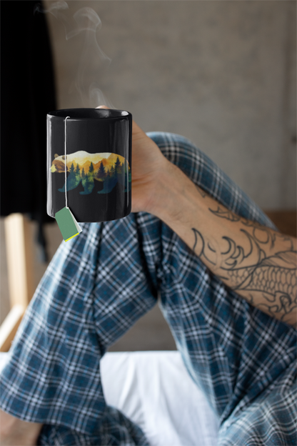 Bear in the Woods Mountain Mug (11 oz, 15 oz) held by a person, showcasing a bear and tree design, ideal for nature lovers. The mug’s rustic theme aligns with FireBrook Essentials' uplifting, nature-inspired products.